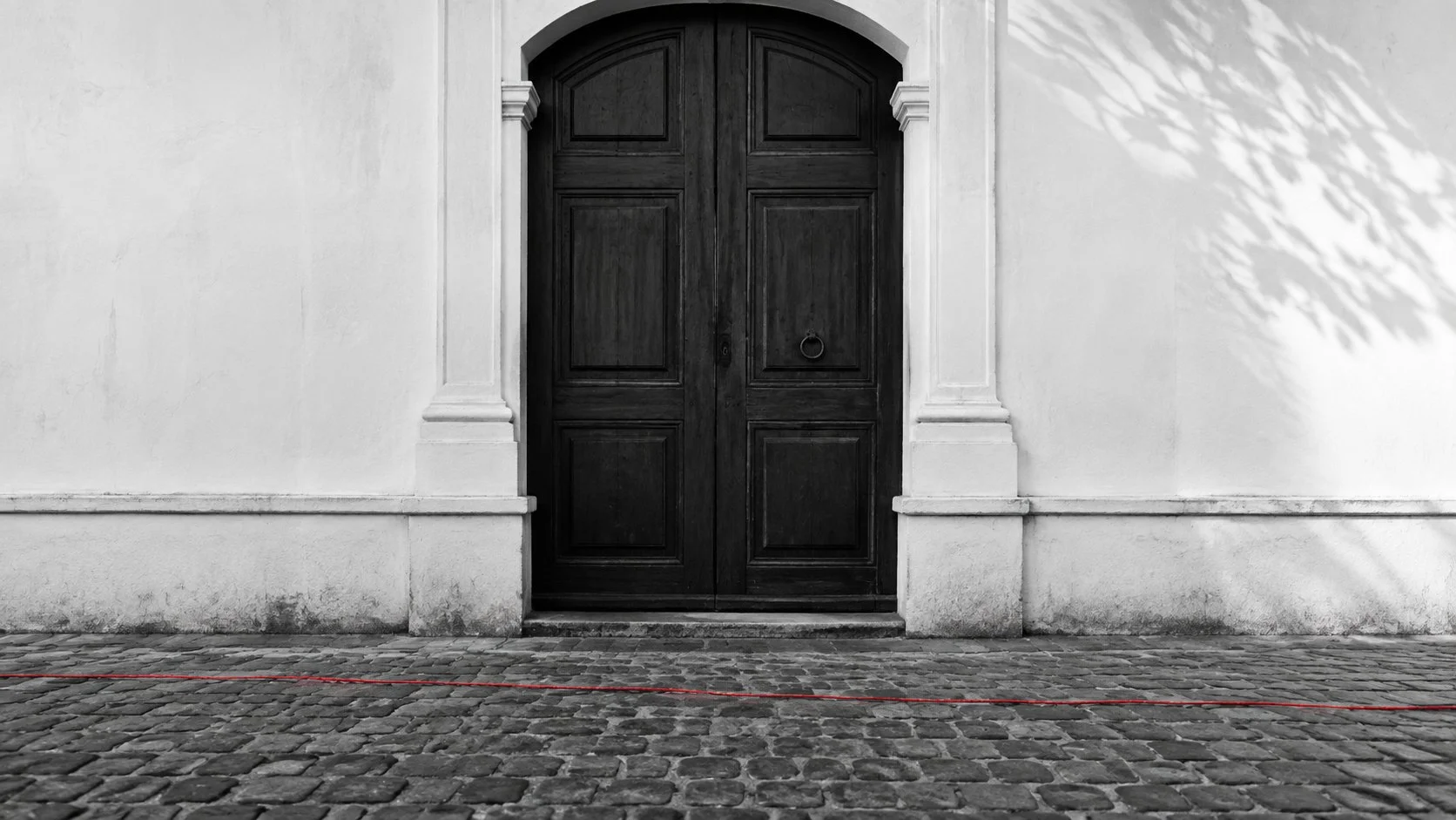Puerta colonial cerrada en Antigua Guatemala, con una línea roja delgada que cruza los adoquines y pasa de largo.