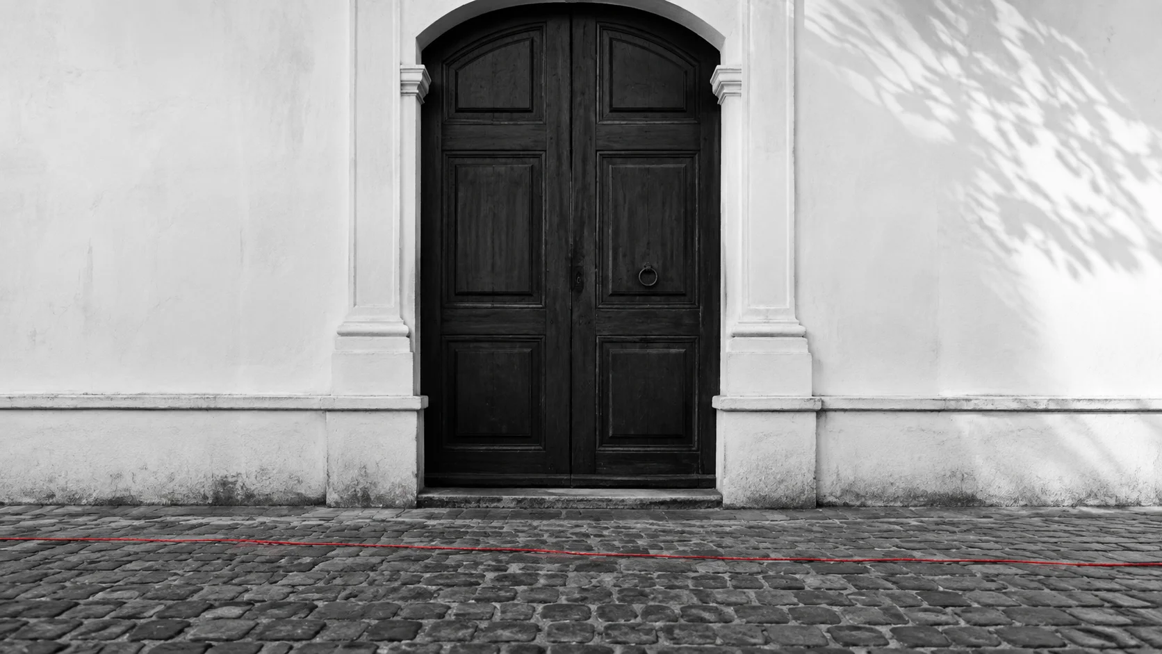 A closed colonial door in Antigua Guatemala, with a thin red line running across the cobblestones and passing it by.